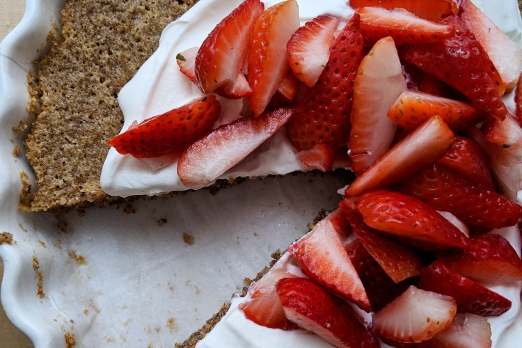 Pecan browned butter cake, topped with whipped cream and strawberries and missing a slice