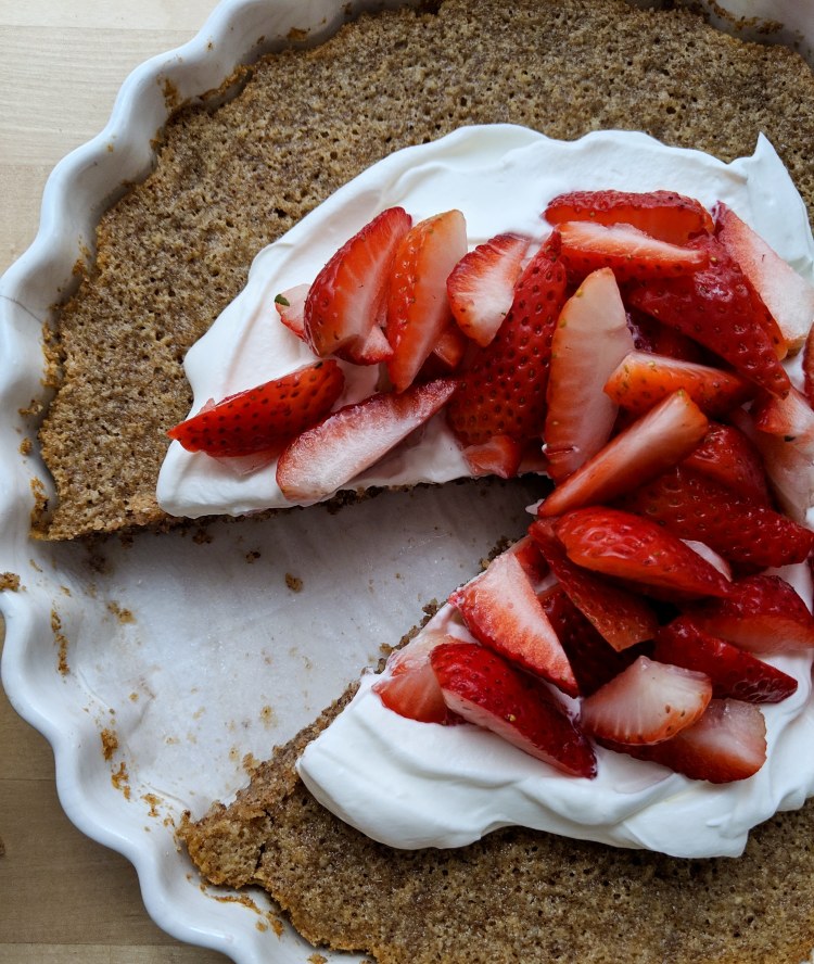 Pecan browned butter cake, topped with whipped cream and strawberries and missing a slice