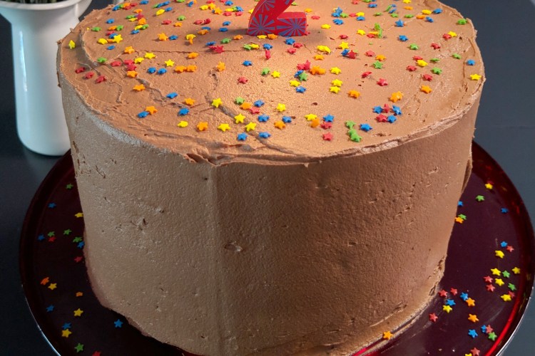 Three-layer cake with chocolate frosting, sprinkles, and a lit candle