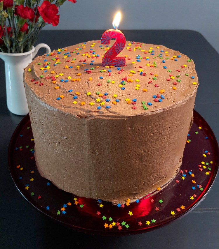 Three-layer cake with chocolate frosting, sprinkles, and a lit candle