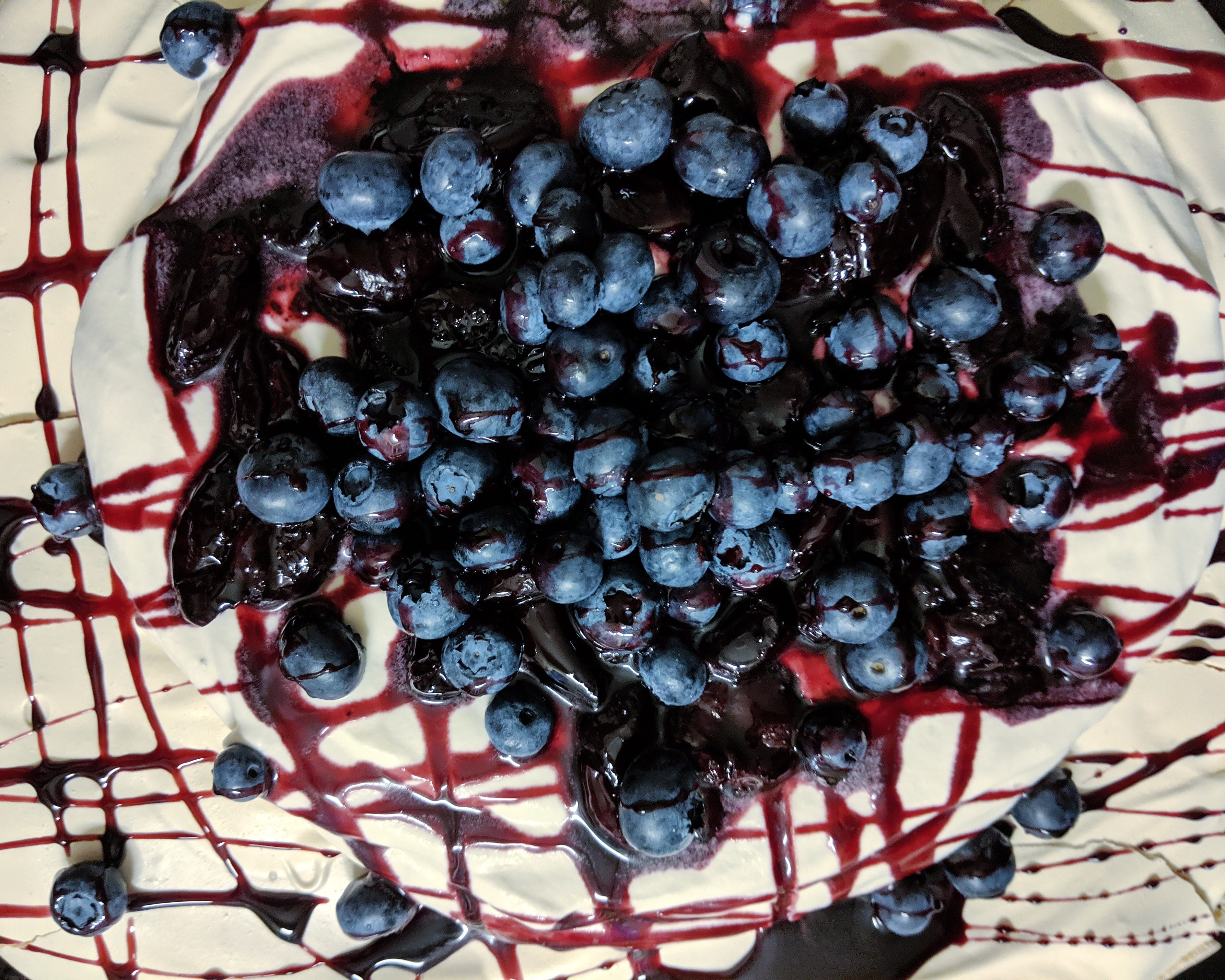 Pavlova topped with whipped cream, roasted cherries, and blueberries