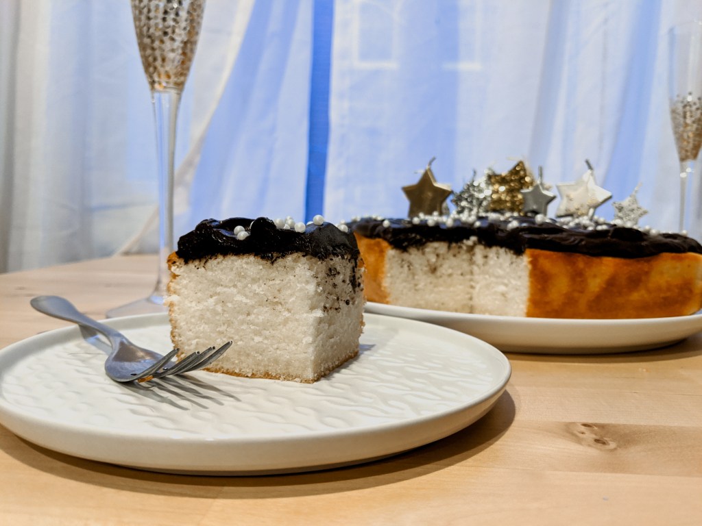 A  slice of white cake with chocolate frosting in front of the remaining cake