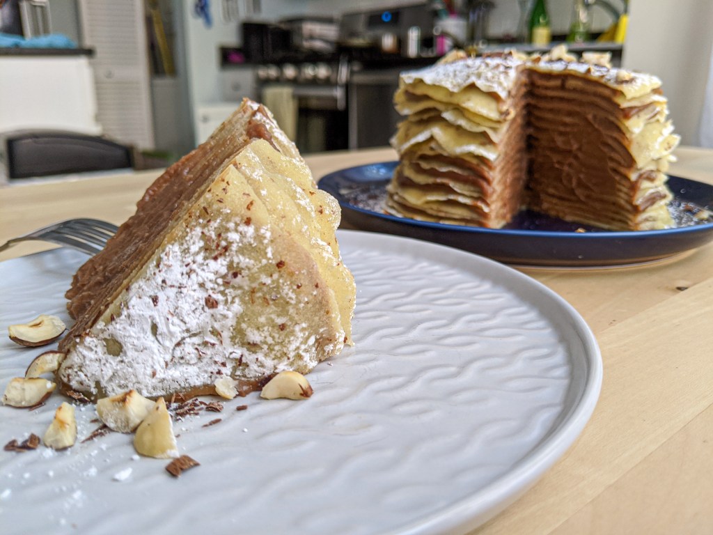 A slice of crepe cake filled with Nutella cream on a plate, with the remaining cake in the background