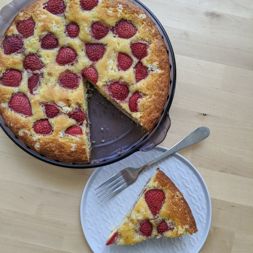 A cake with strawberries baked into the top with a slice cut out and sitting next to it.