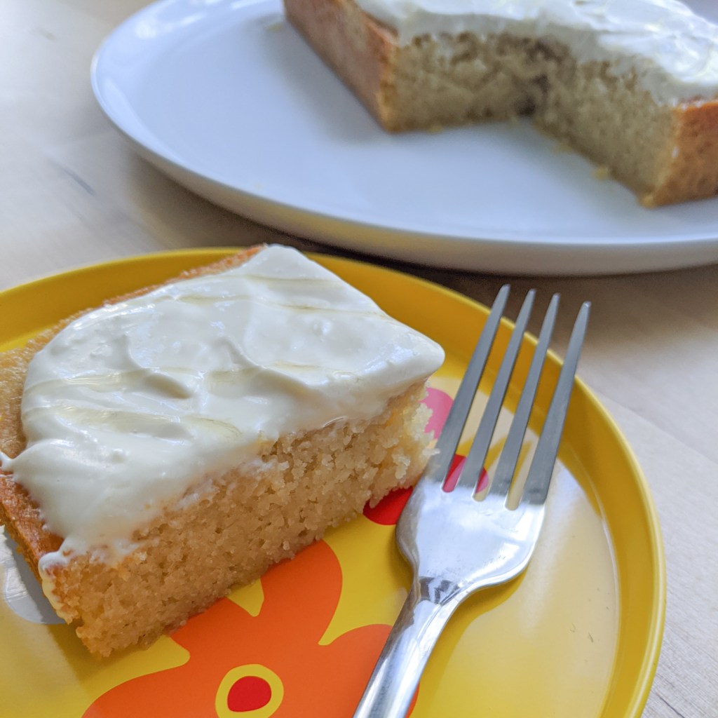 A square of honey cake with cream cheese frosting on a yellow plate