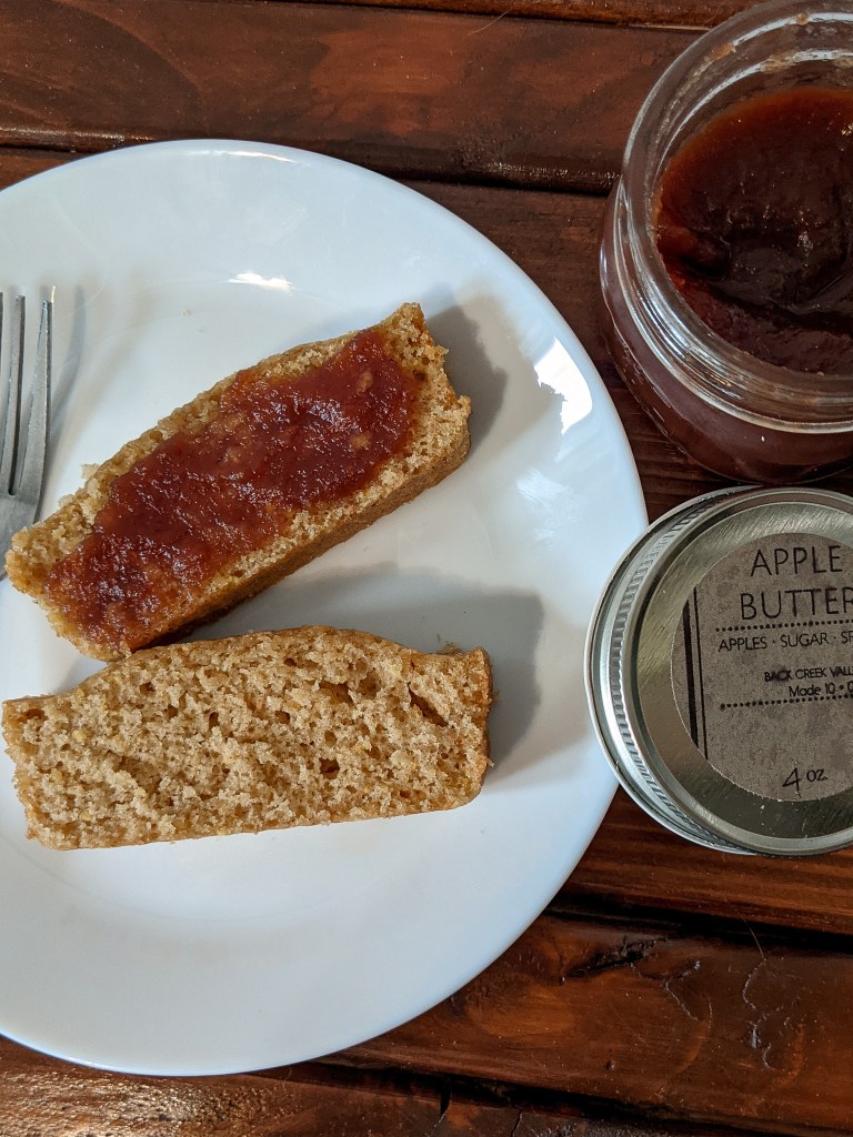 Two slices of brown sugar cake, one with apple butter spread on top, with a jar of apple butter open next to the plate