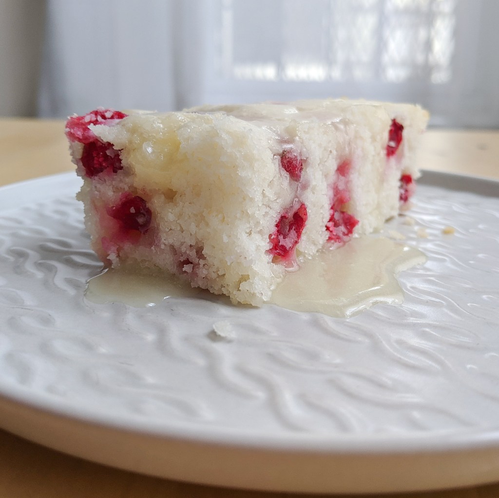 A white cake studded with bright red cranberries and coated in butter sauce