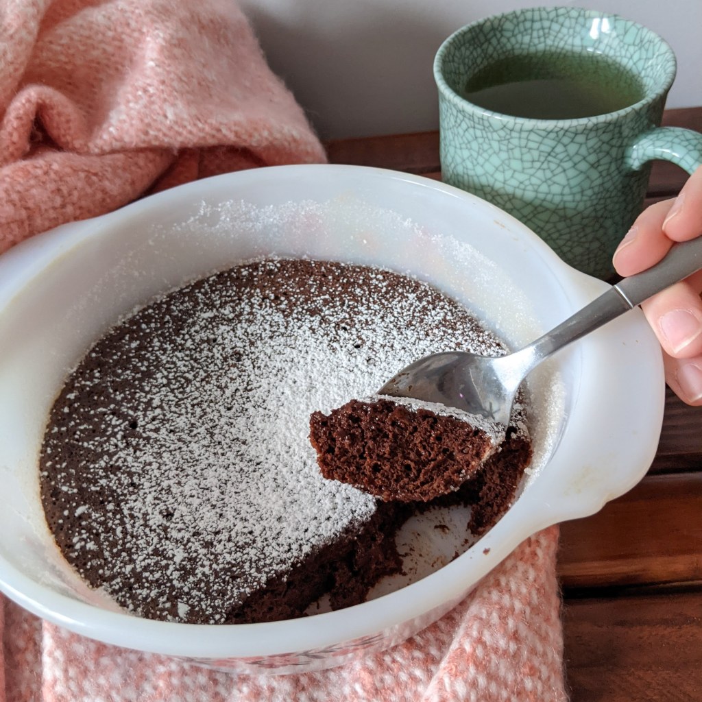 A pan of chocolate pudding cake, with a scoop being taken out and a mug of tea nearby.