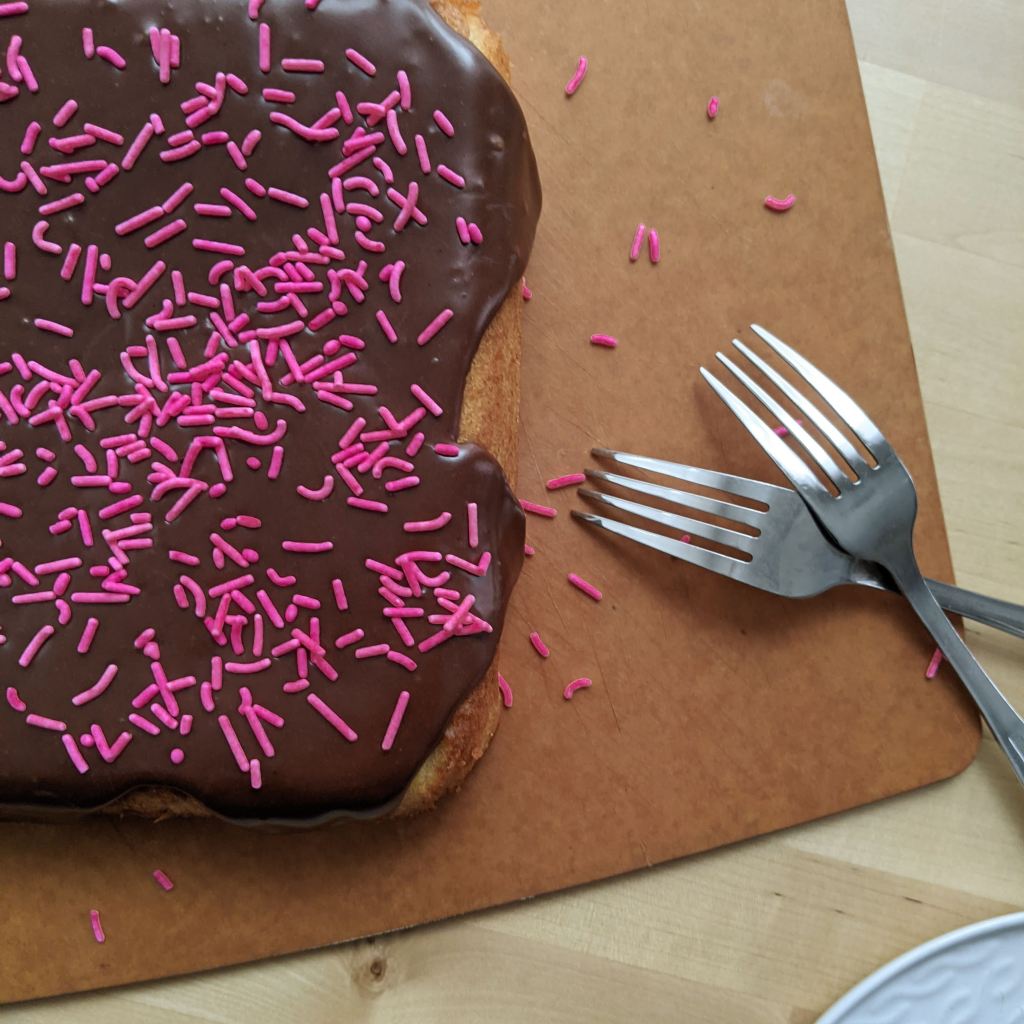 A chocolate-glazed cake with pink sprinkles on top and two forks resting next to it