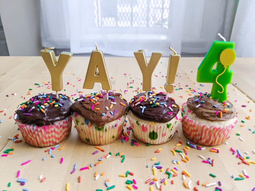 Four chocolate-frosted cupcakes with candles that read "YAY!" and a #4 candle with a balloon on it.