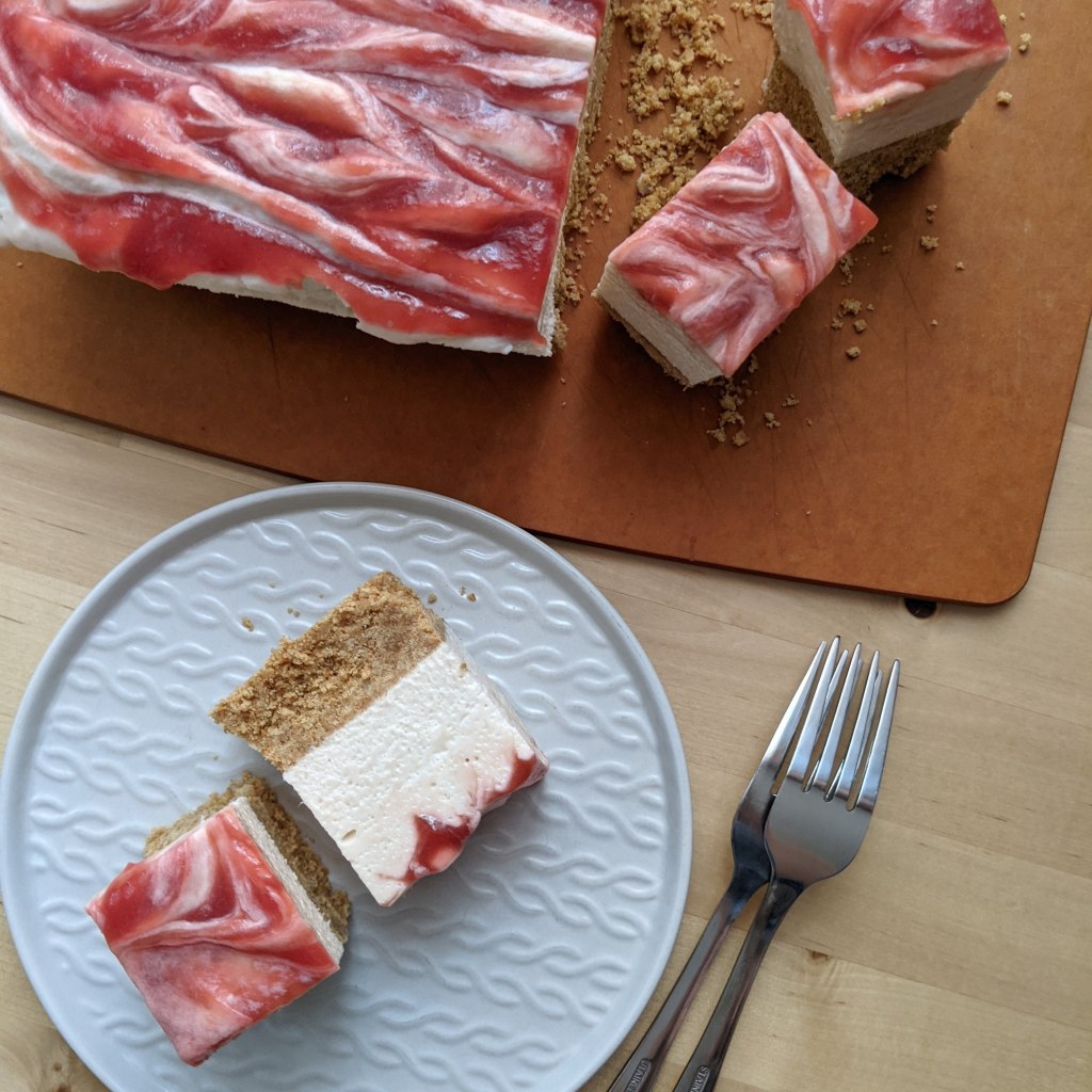 Two tall slices of rhubarb-swirled cheesecake on a plate alongside the remaining cake on a cutting board.